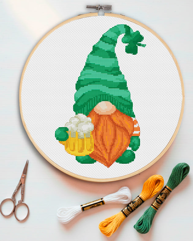 Embroidery hoop with a Patrick Day gnome design, cross-stitch threads, and scissors on a light background