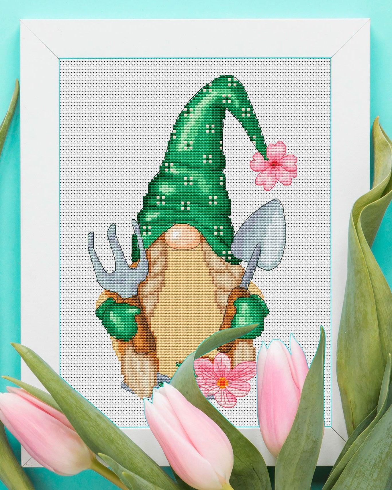 Cross-stitched spring gnome with a green hat and pink flowers on a turquoise background