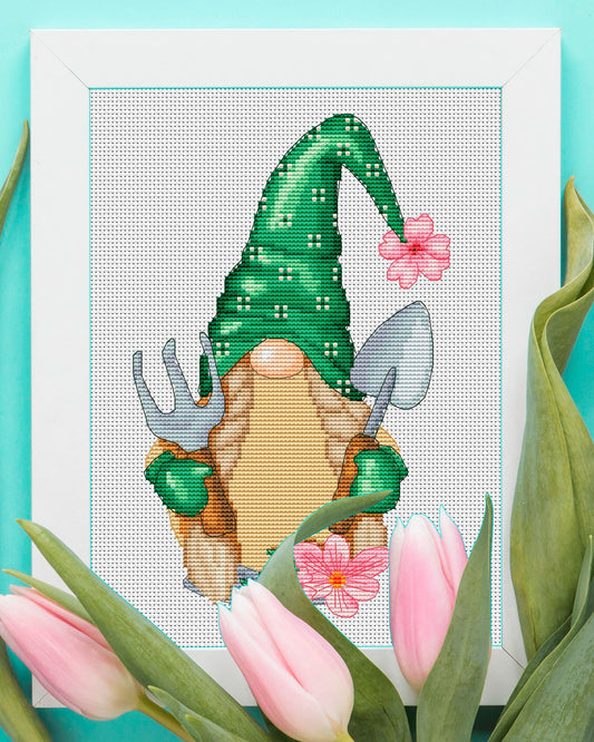 Cross-stitched spring gnome with a green hat and pink flowers on a turquoise background