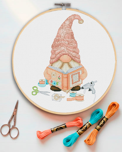 Cross stitch pattern of a Scrapbook Gnome sitting with an album. Cute gnome embroidery design themed with crafting accessories: scissors, tapes, and glue gun. Digital PDF pattern for craft room decor.