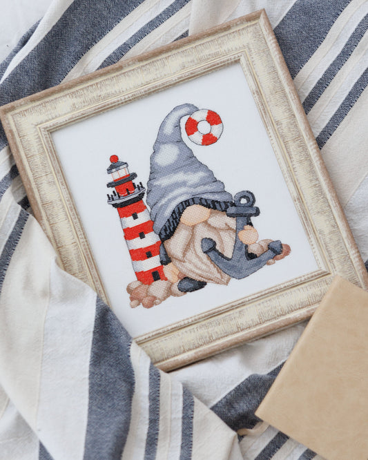 Framed cross-stitched picture of a gnome with a lighthouse on a striped fabric background