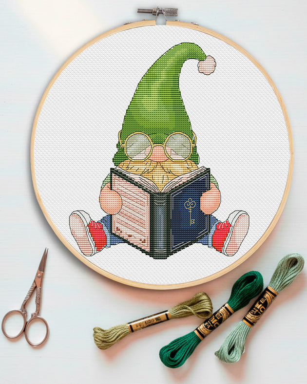 Book gnome cross stitch pattern preview — gnome in green hat reading a book with round glasses, DMC cross stitch chart — CuteBroidery

