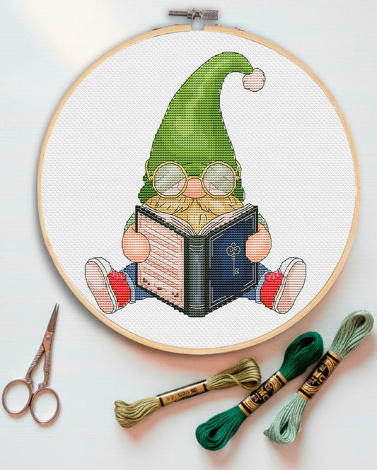 Book gnome cross stitch pattern preview — gnome in green hat reading a book with round glasses, DMC cross stitch chart — CuteBroidery
