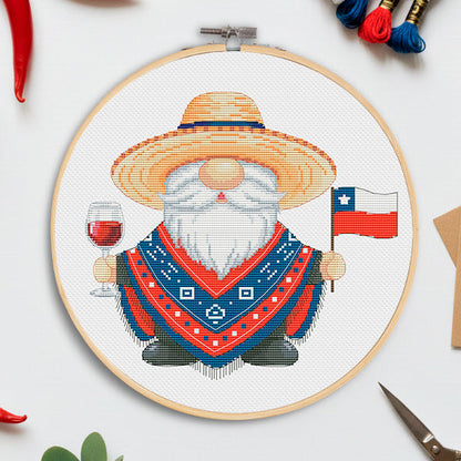 Embroidery hoop with a gnome design holding a Chilean flag and glass of wine, surrounded by red peppers and embroidery threads.