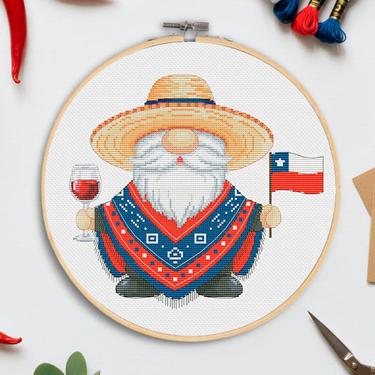 Embroidery hoop with a gnome design holding a Chilean flag and glass of wine, surrounded by red peppers and embroidery threads.