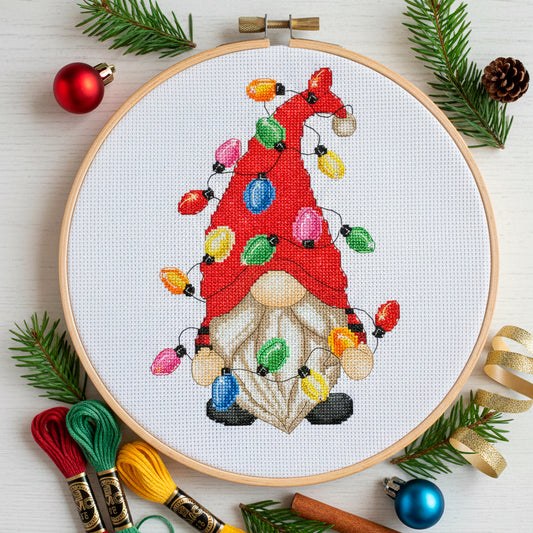 Cross-stitched gnome with Christmas lights in an embroidery hoop, surrounded by festive decorations. PDF pattern