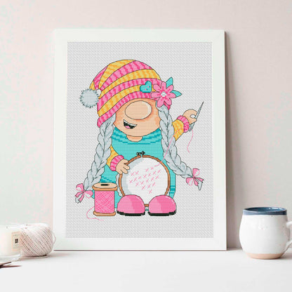 Stitching gnome girl cross stitch displayed in embroidery hoop with colorful pom pom trim 