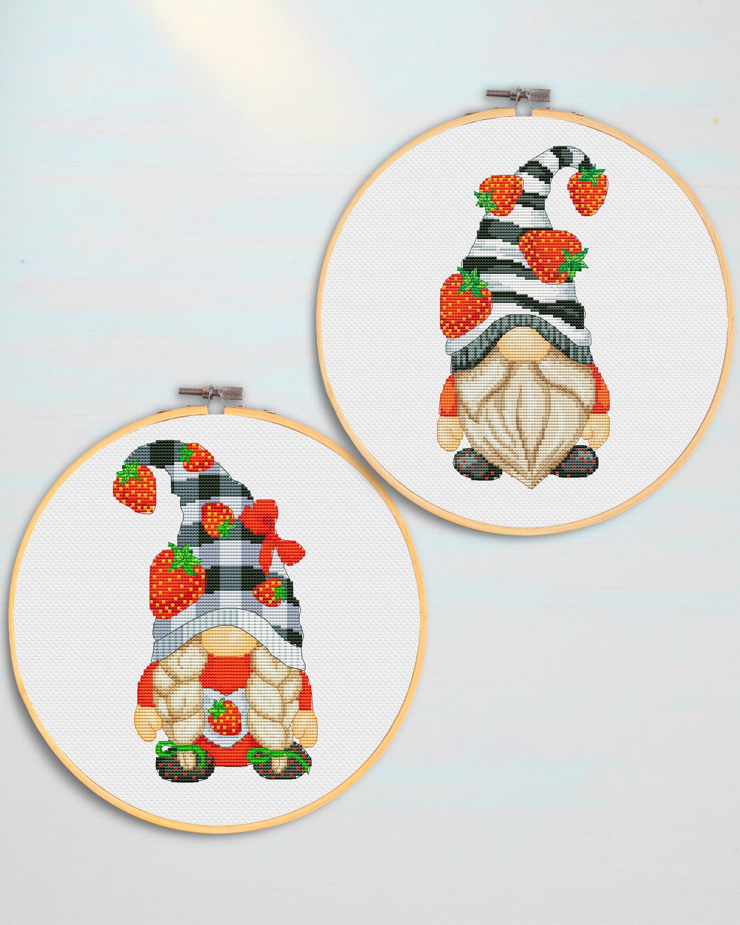 Two cross-stitched gnomes in embroidery hoops on a light blue background
