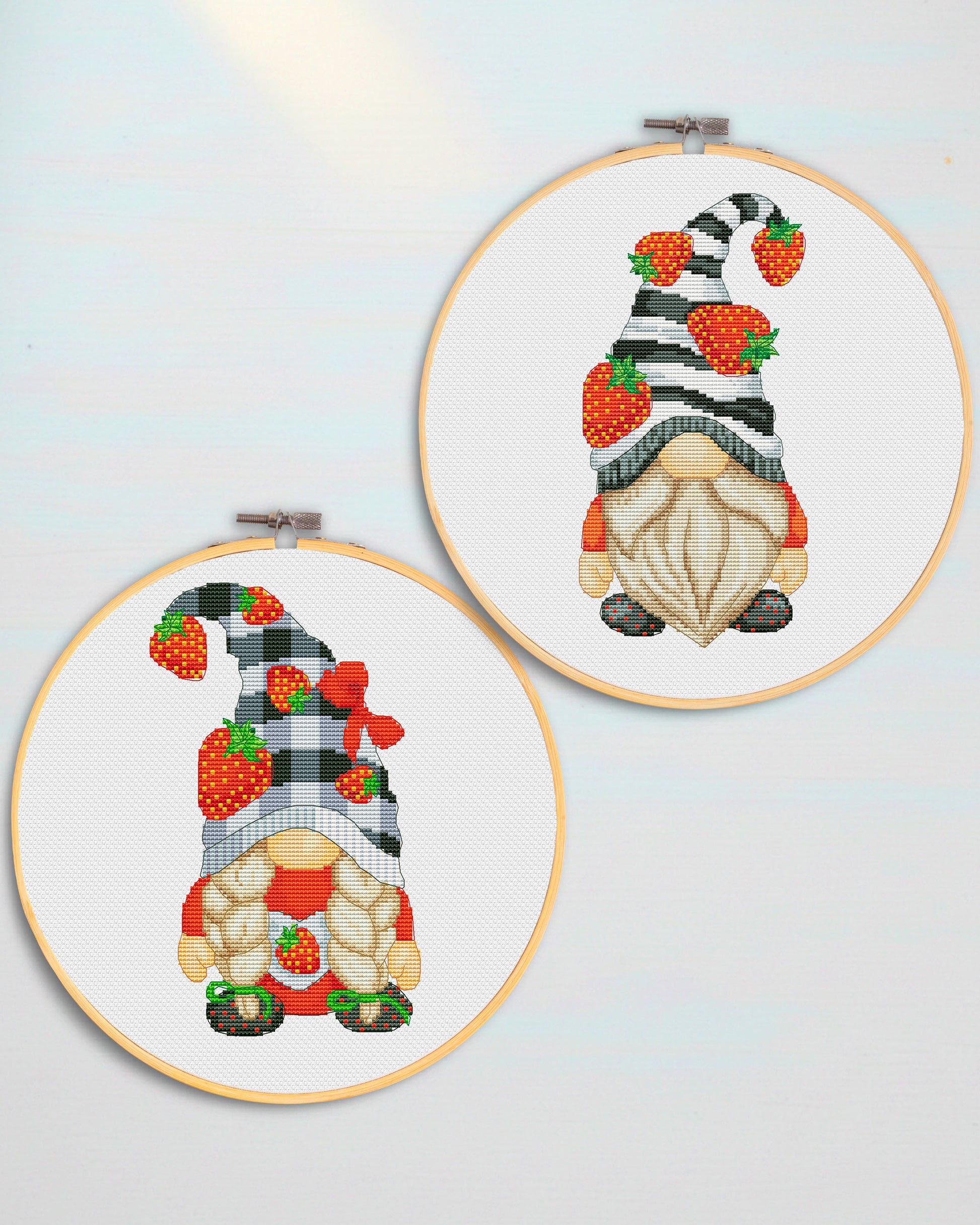 Two cross-stitched gnomes in embroidery hoops on a light blue background